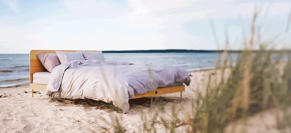 summer_breeze_landscape | Kaissu Store Online Wooden bed with white linens and pillows on a sandy beach by the ocean.